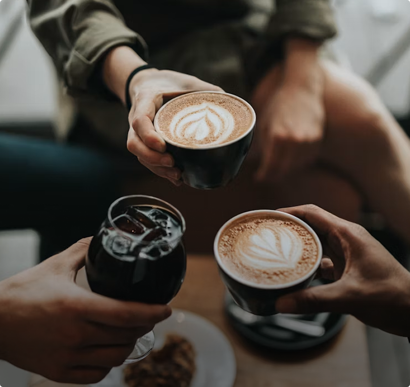 Hands holding coffee drinks, including two lattes with latte art, in a cozy café setting
