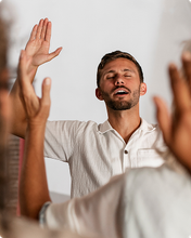 Man with eyes closed and raised hand, worshipping in a bright indoor setting