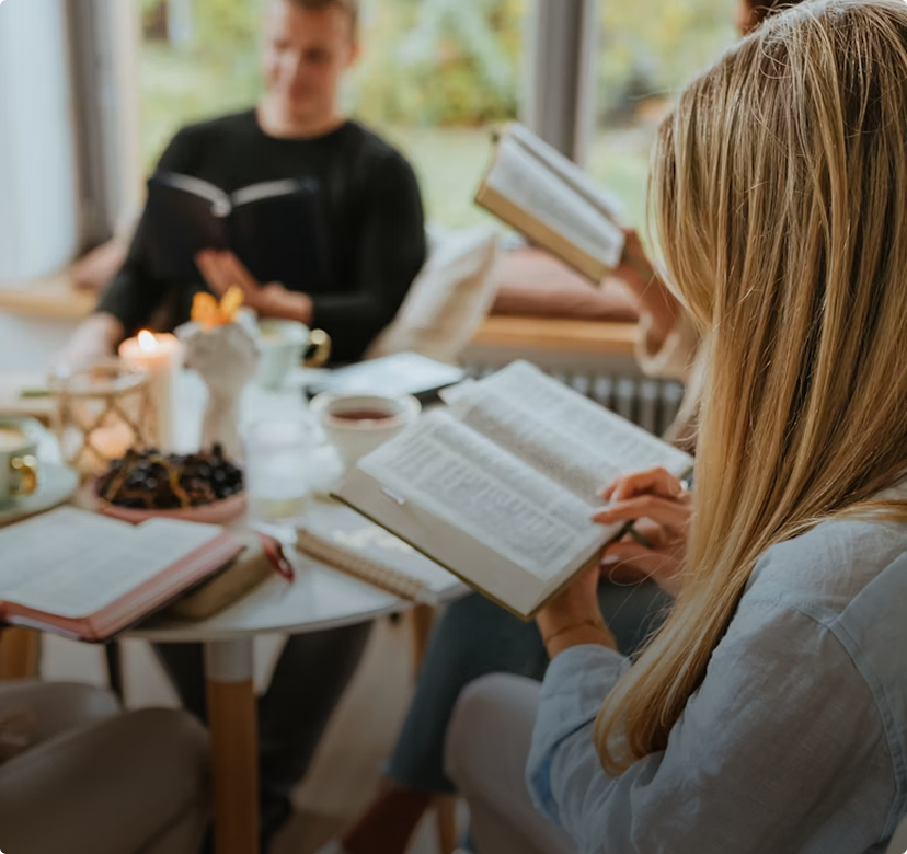 People reading books together at a table in a bright indoor room