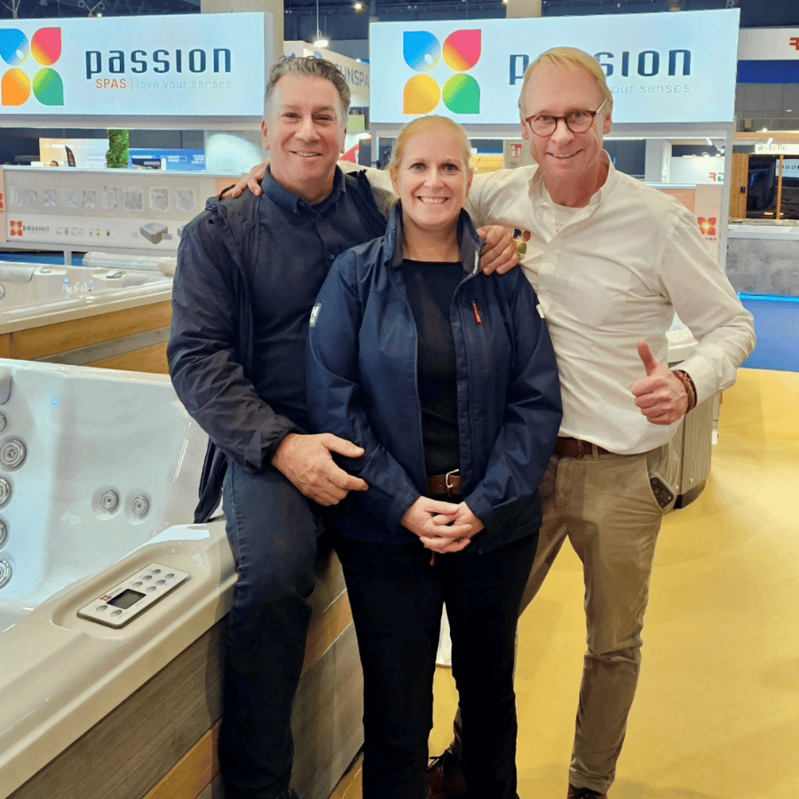 Three people smiling at a jacuzzi showroom, standing beside a white spa tub.