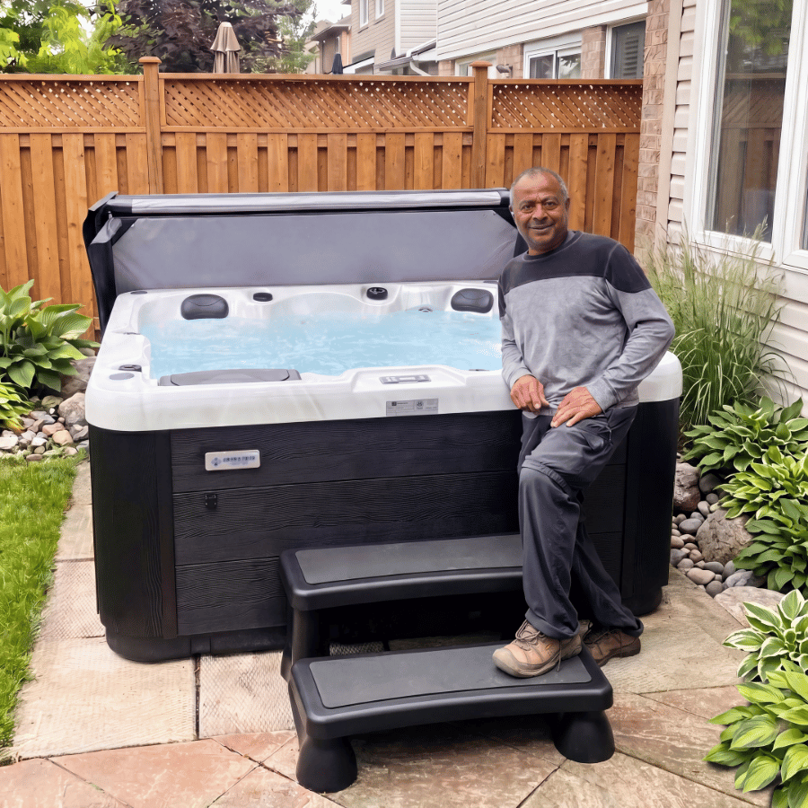 Man sitting beside a black-and-white hot tub in a fenced backyard