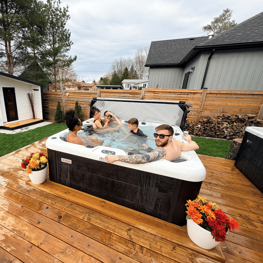 People relaxing in a backyard hot tub on a wooden deck, with flowers and a fence around them