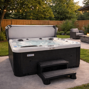Backyard hot tub with steps and cover, set on a patio beside outdoor seating.