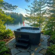 Backyard hot tub on stone patio overlooking a misty lake and pine trees at sunrise