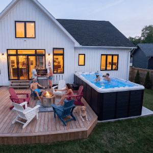 Backyard deck with fire pit, lounge chairs, and an above-ground pool beside a white house at dusk