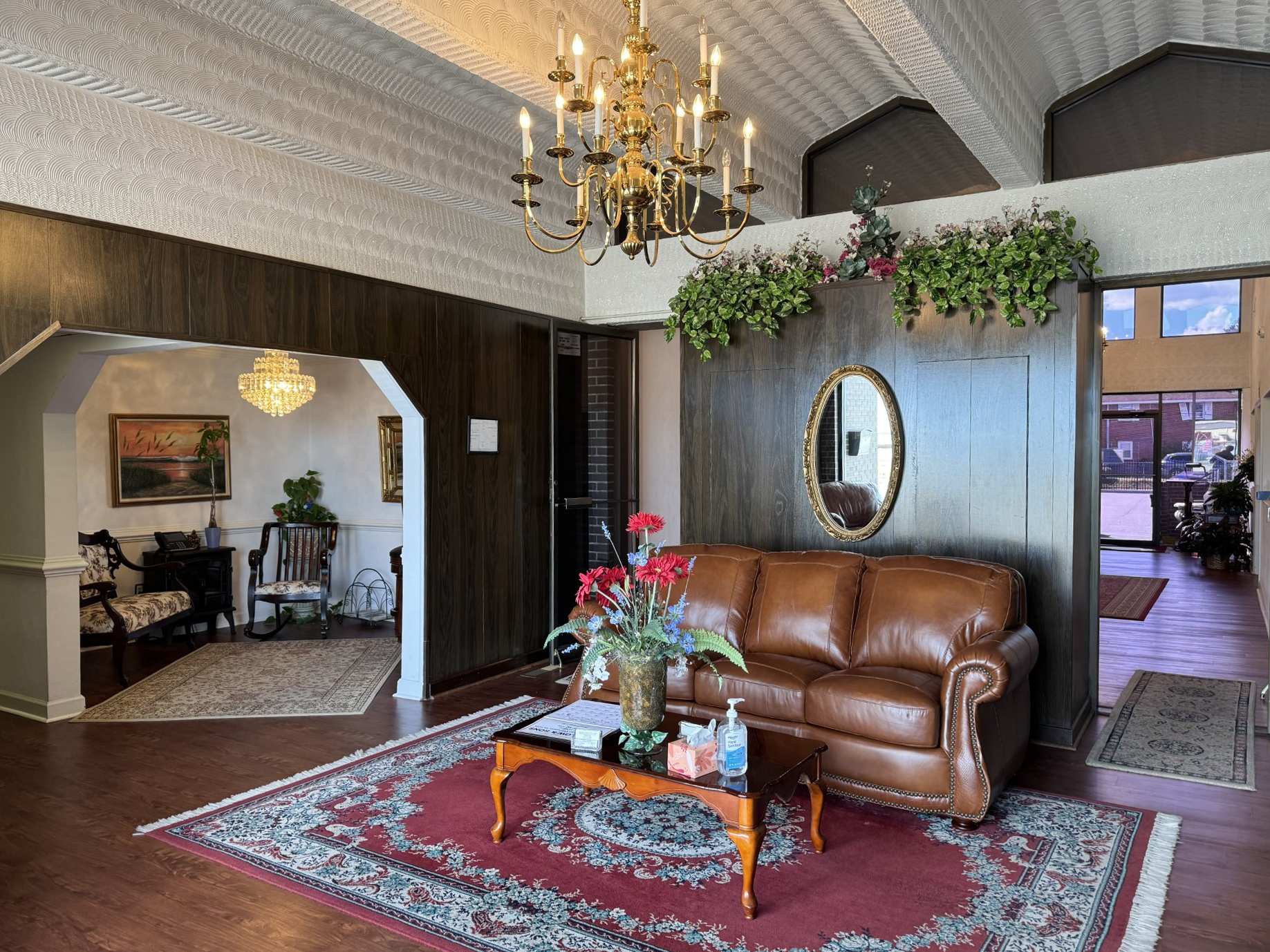 Lobby with brown leather sofa, red rug, chandelier, and a hallway leading to another room.