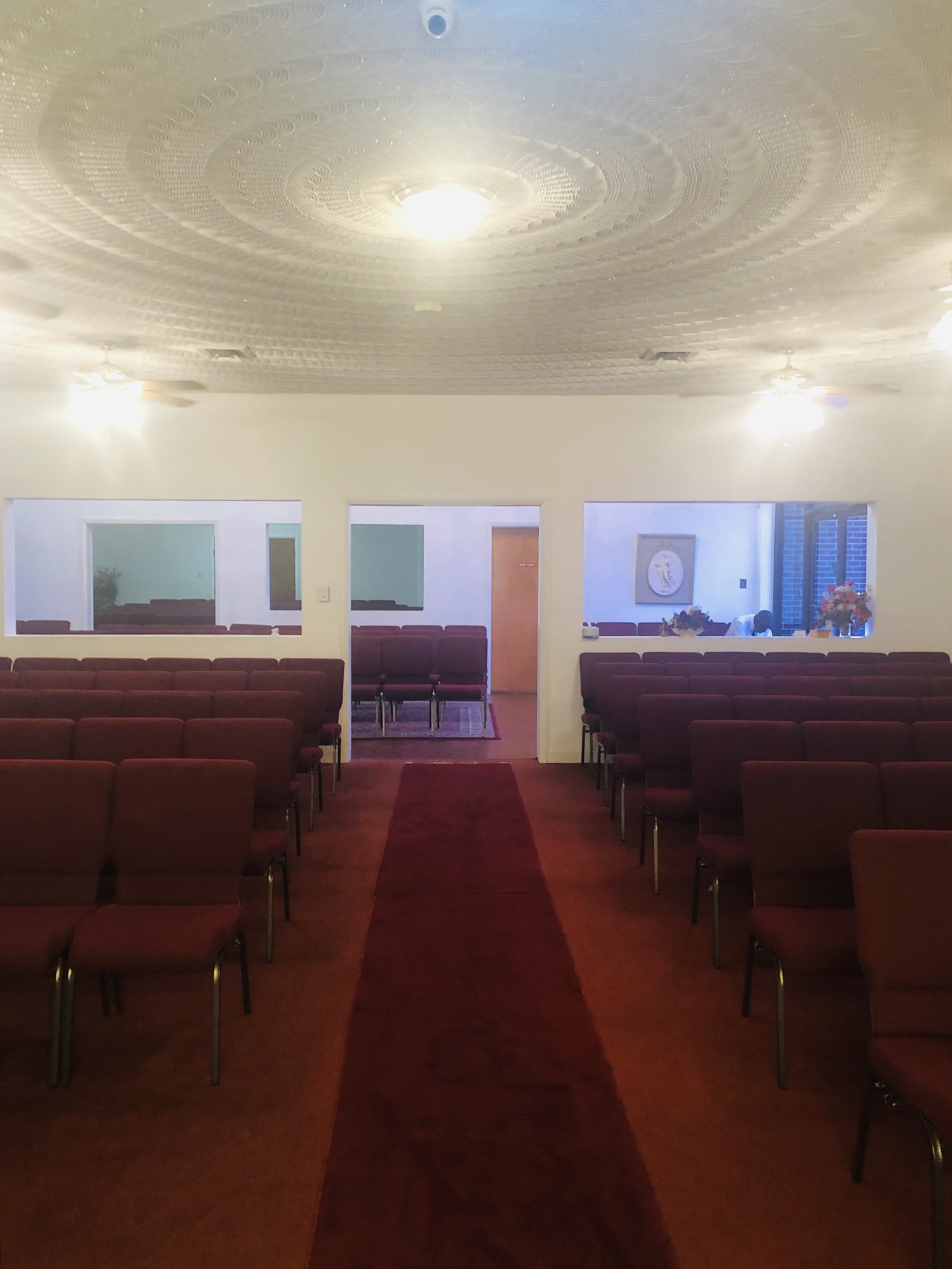 Inside a chapel, red carpet aisle, rows of red chairs, open doorways, circular ceiling design.