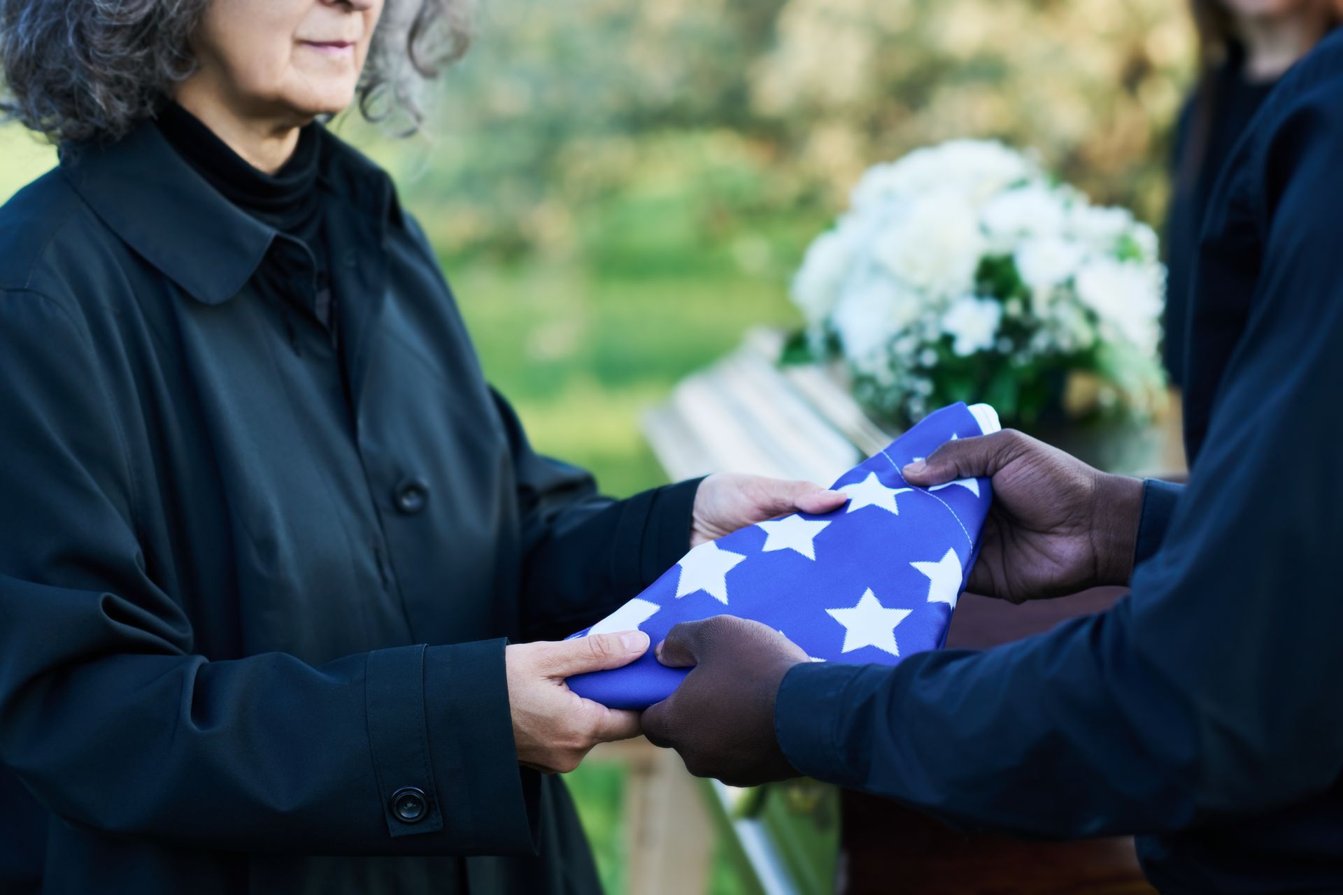Person in black coat receives folded American flag at a funeral.