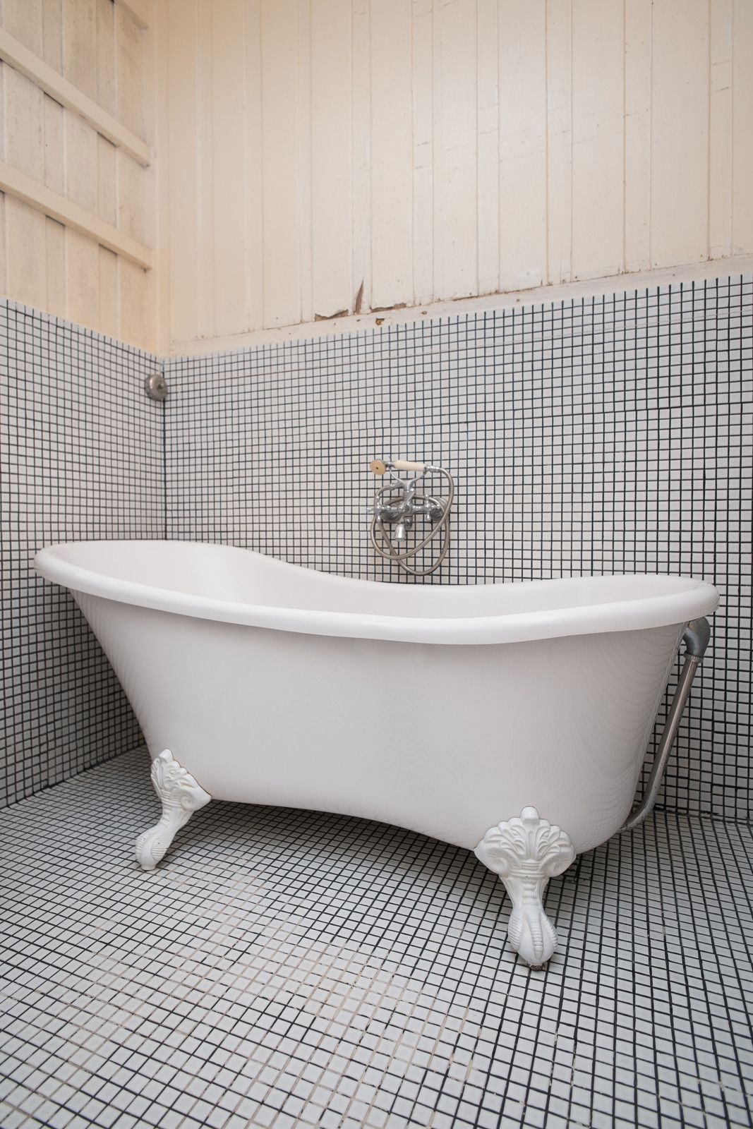 White clawfoot bathtub in a tiled bathroom with light wood-paneled walls.