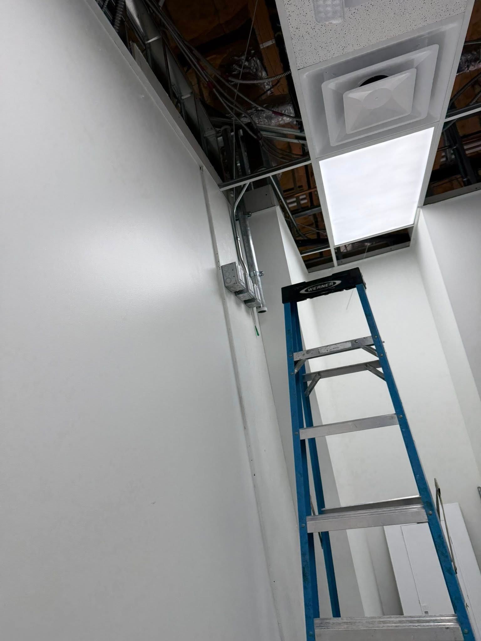 Blue ladder against white walls, near ceiling with vent and exposed wiring.