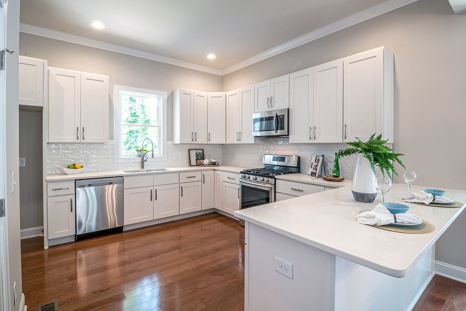 White kitchen with stainless steel appliances, white cabinets, and a white countertop island on wood floors.