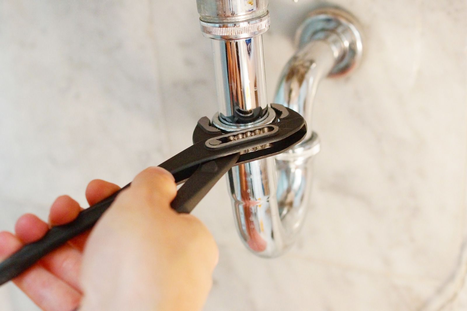 Hand using a wrench to tighten a chrome sink pipe under a bathroom sink