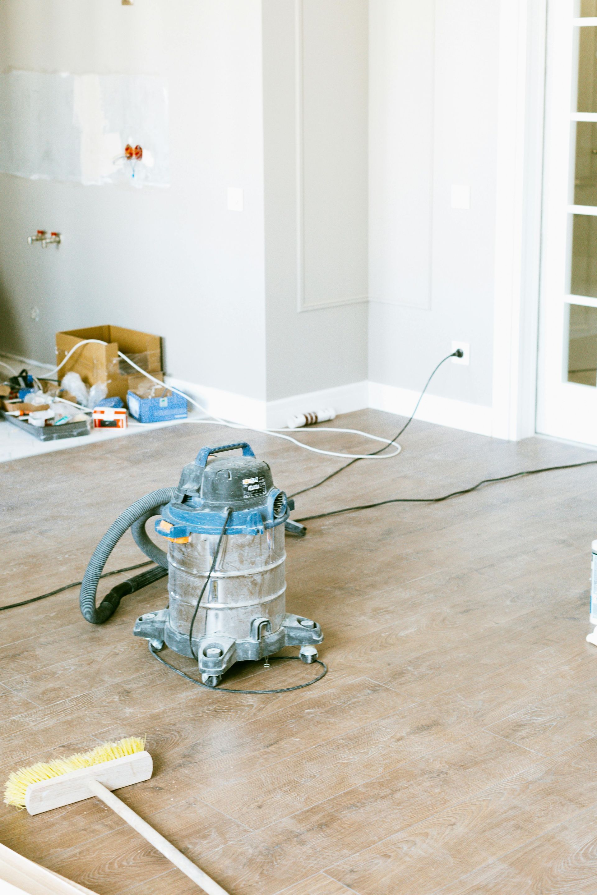 A vacuum cleaner sits on a dusty floor in an unfinished room during renovation.