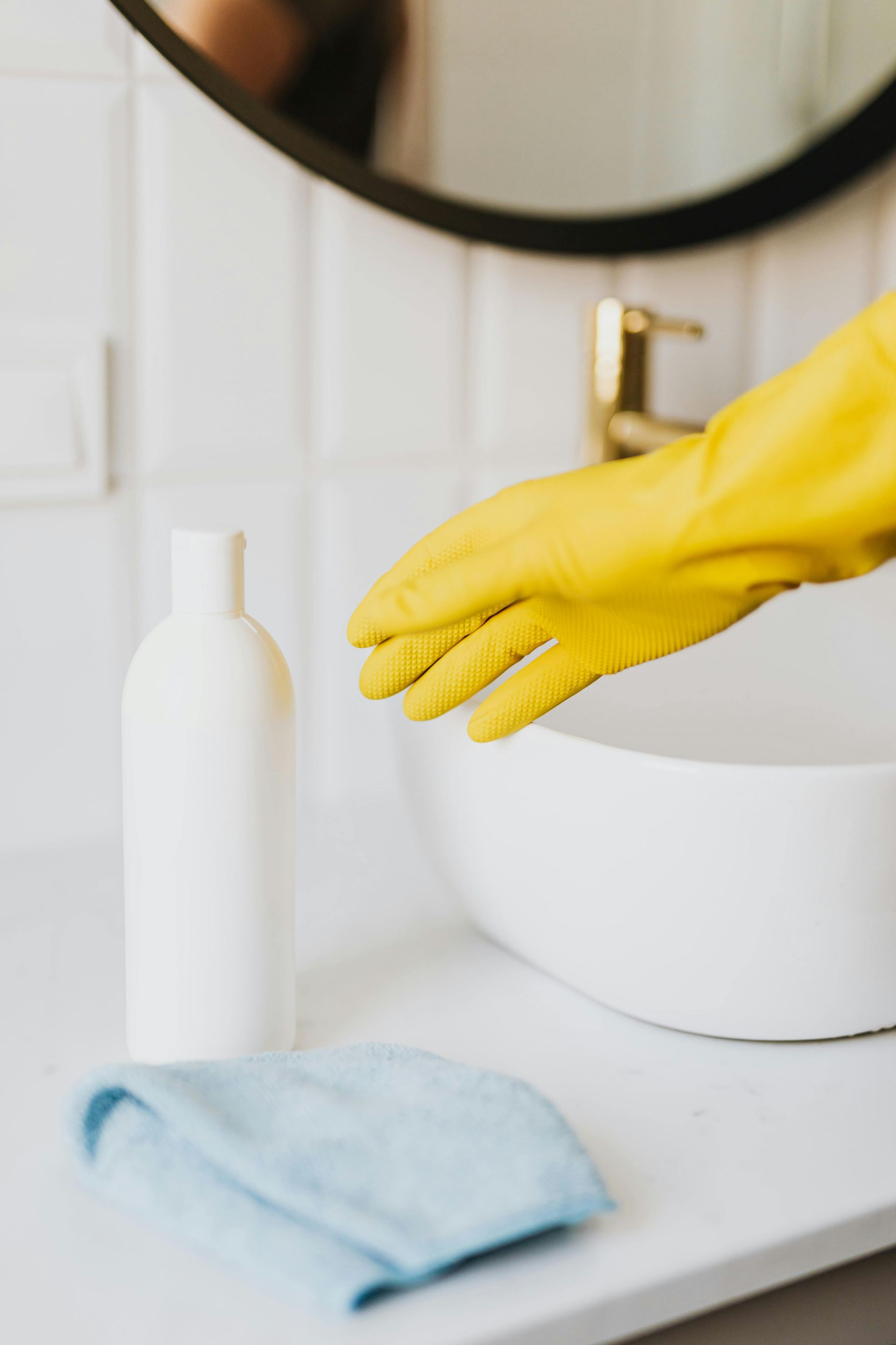 Yellow cleaning gloves over a bathroom sink with a white bottle and folded blue cloth