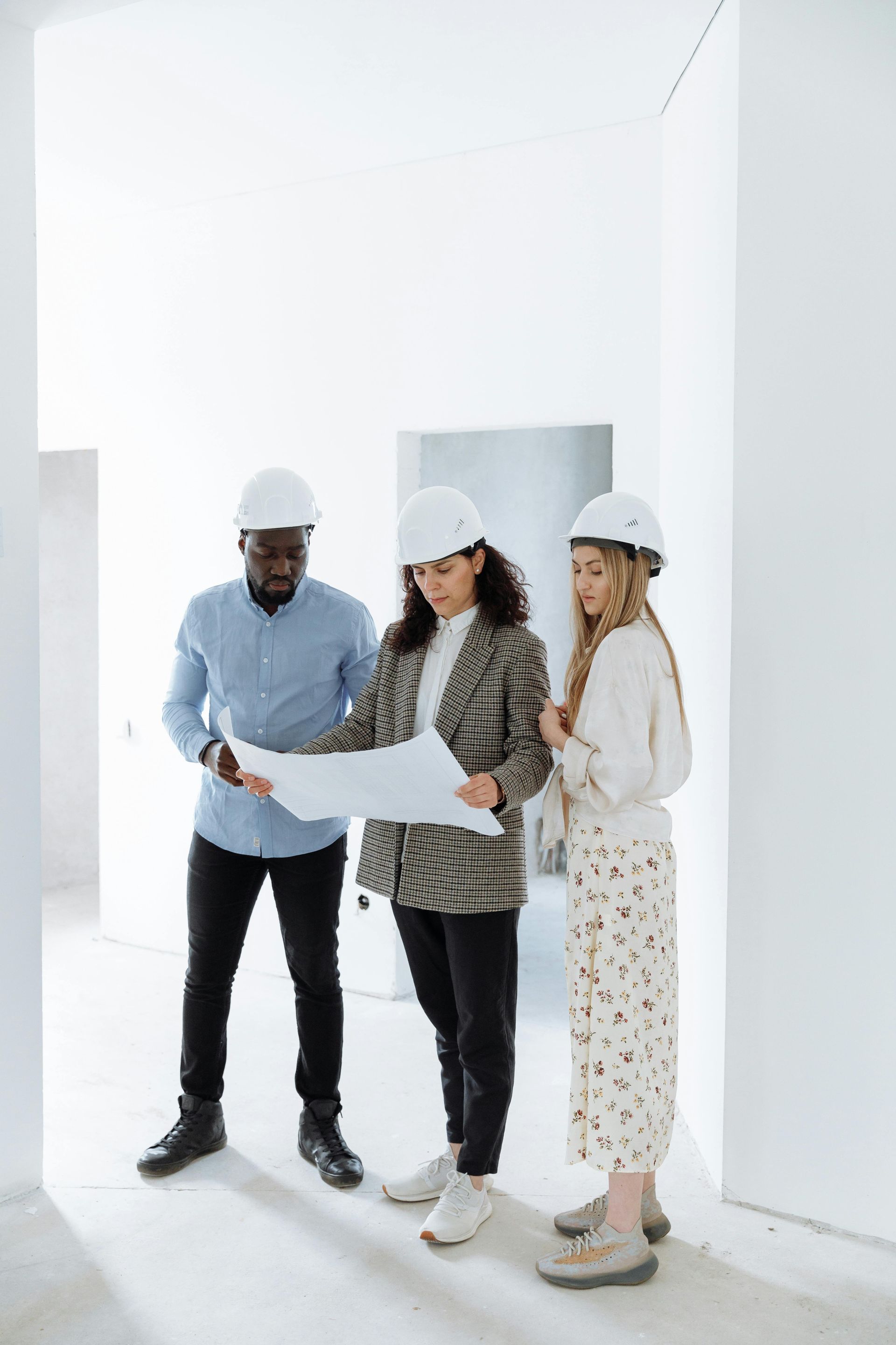 Three people in hard hats reviewing building plans in a bright unfinished room