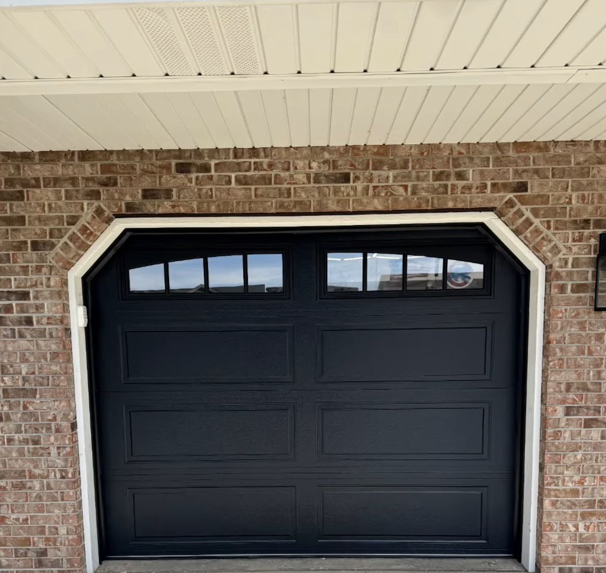 Two-car garage with white doors and a brick driveway in front of a house