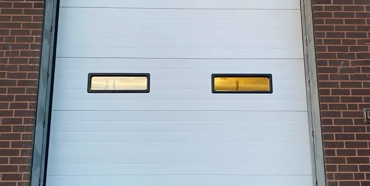 White garage door with two narrow windows, framed by brick walls.