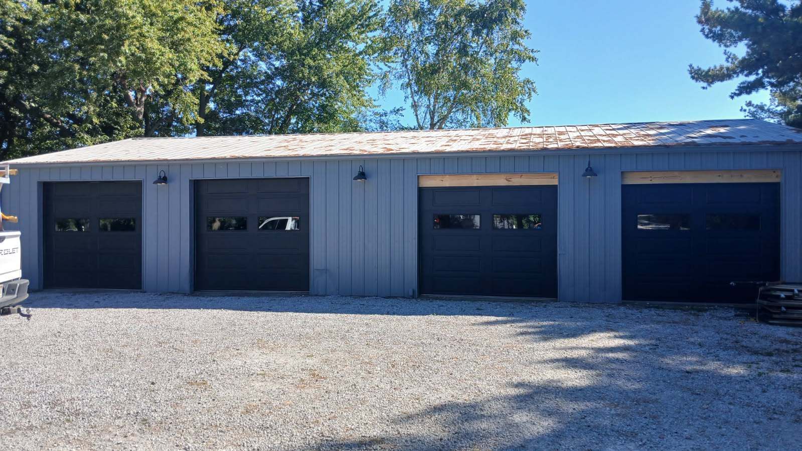 Brick industrial garage with three large black doors and yellow bollards under a blue sky