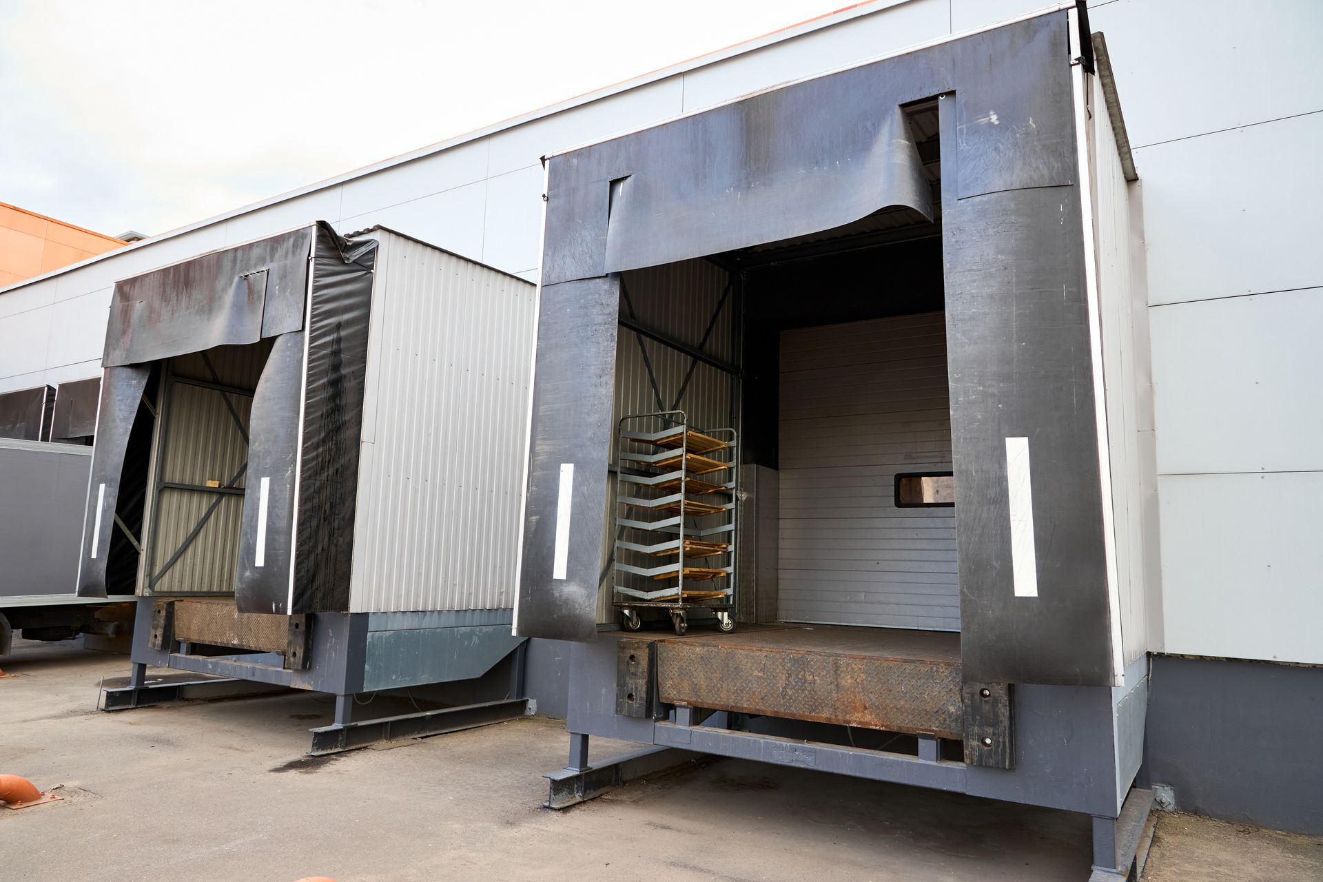 Two large industrial loading dock trailers with open rear doors, one holding stacked trays.
