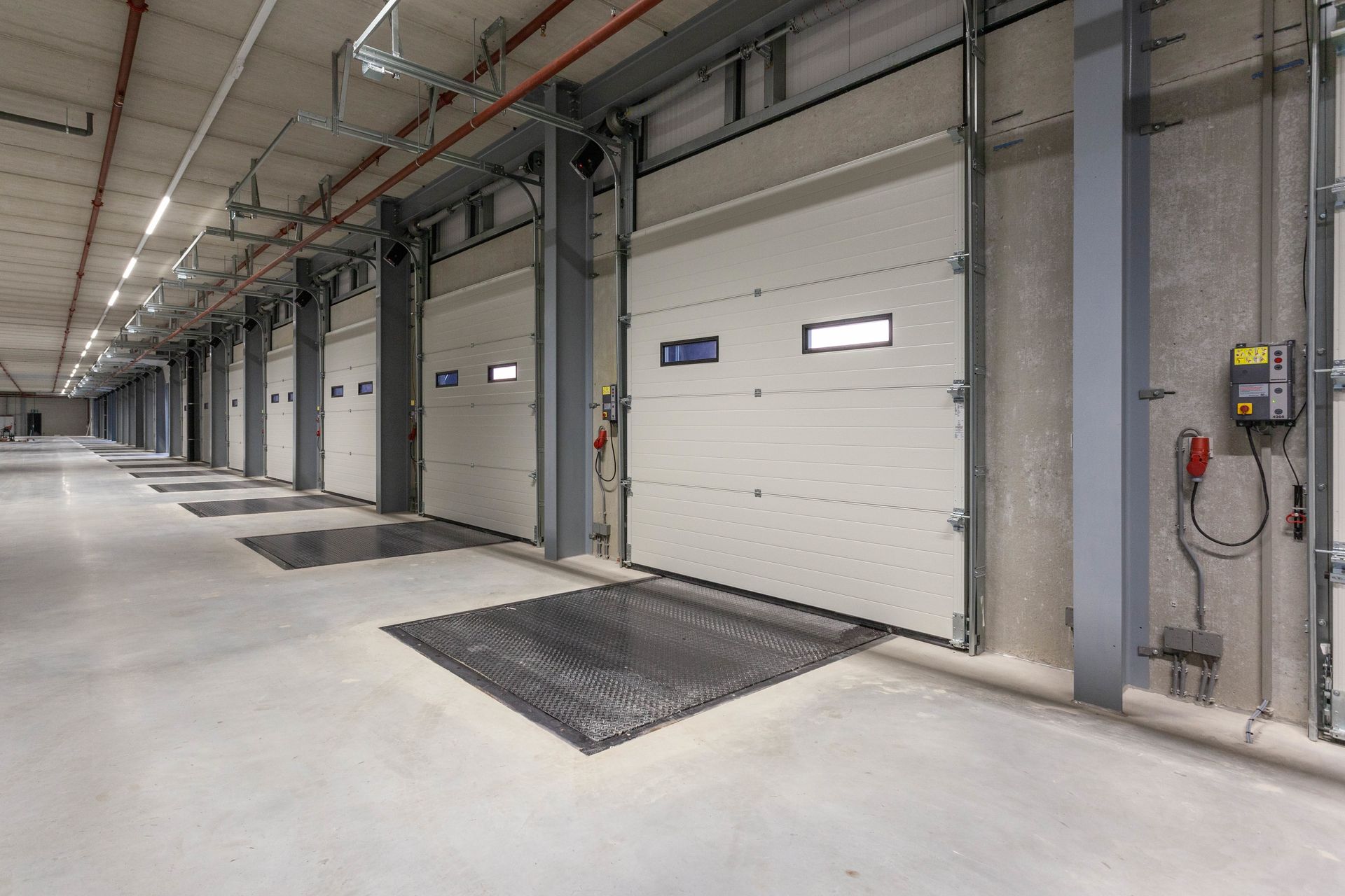 Industrial warehouse corridor with large white dock doors, concrete floor, and overhead lighting
