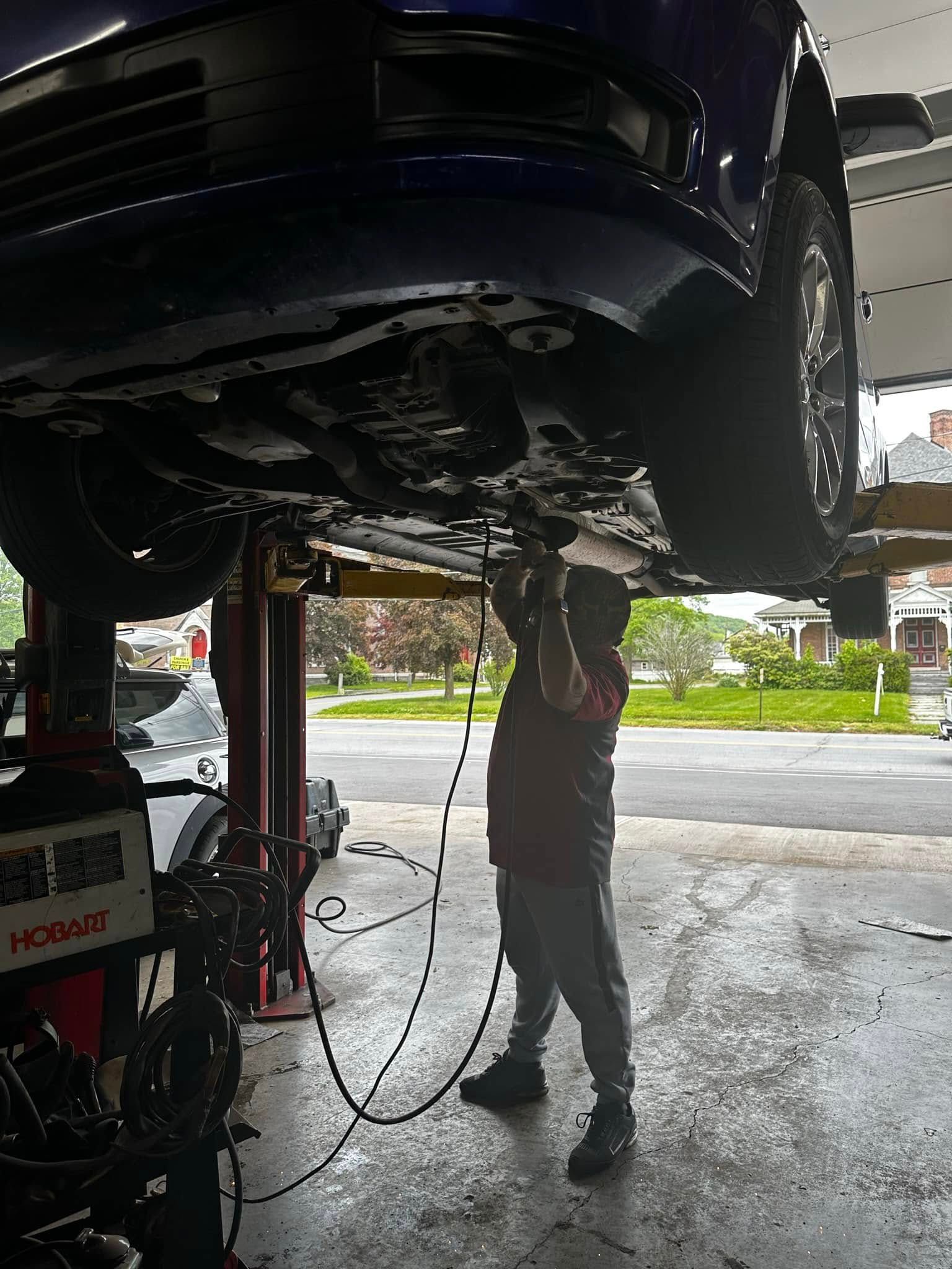 Mechanic inspecting a lifted black car’s undercarriage in a garage, with tools and hoses nearby | 1st Class Alignment & Repair