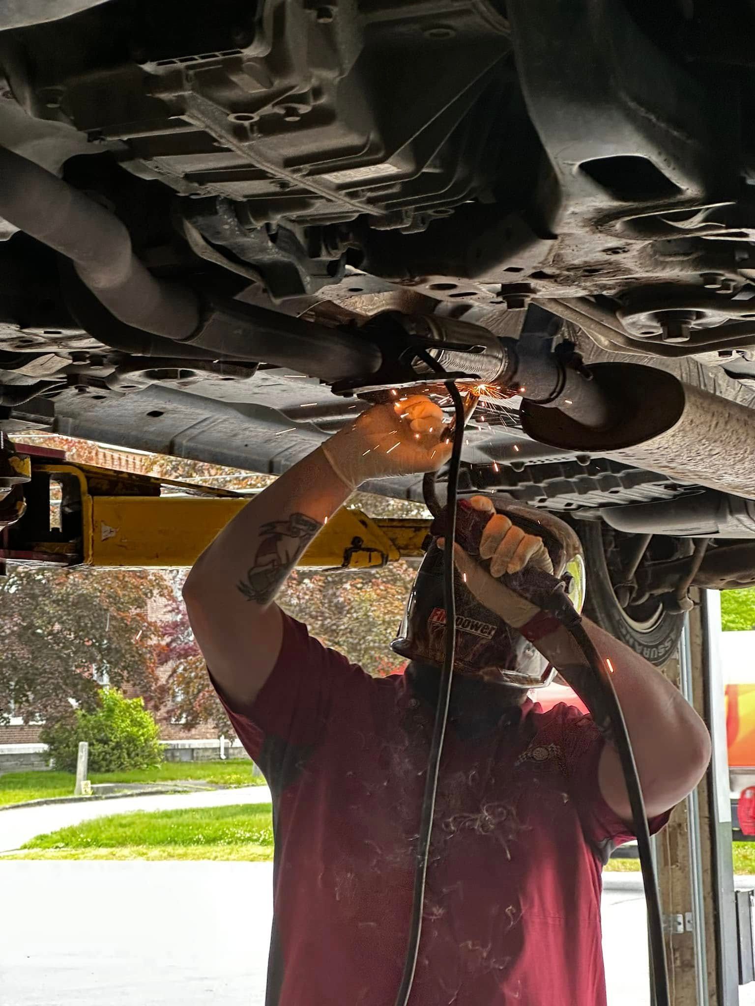 Mechanic working under a vehicle, using a tool near the engine area. | 1st Class Alignment & Repair