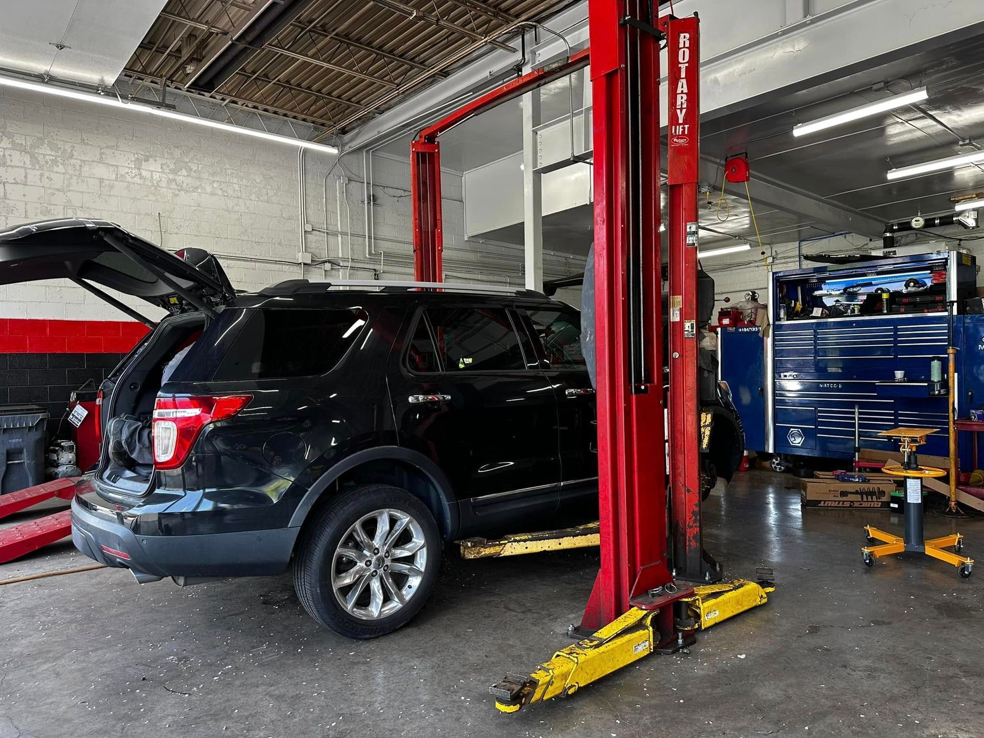 Black SUV on a lift in an auto repair shop, with the hood open and tool carts nearby. | 1st Class Alignment & Repair