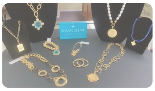 Gold and turquoise jewelry display on black stands with a blue Susan Gale card in the center