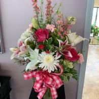 Pink and white flower arrangement with lilies, daisies, and a plaid ribbon bow