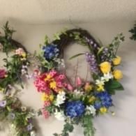 Floral wreaths with colorful artificial flowers hanging on a wall, including blue, yellow, pink, and white blooms