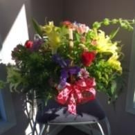 Colorful flower bouquet with red ribbon in a vase on a chair near a sunlit wall