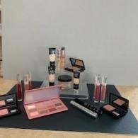 Assorted makeup products and palettes arranged on a table against a plain wall.