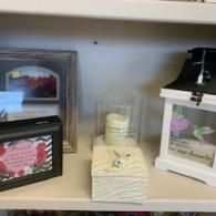 Shelf with framed art, a glass candle, stacked napkins, and a tissue box with flowers.