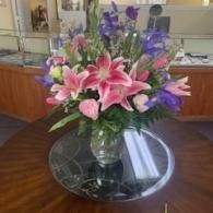 Pink and purple flower arrangement in a glass vase on a round table in a lobby
