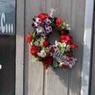 Red and white floral wreath with a “Welcome” sign hanging on a weathered wooden door
