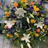 Floral funeral wreath with white lilies, orange and purple flowers, and green foliage