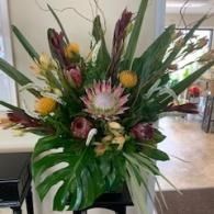 Colorful tropical floral arrangement with green leaves, pink and yellow blooms, on a table indoors