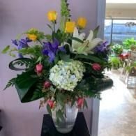 Colorful flower arrangement with purple, yellow, white, and pink blooms in a glass vase indoors