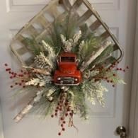 Red truck wreath with frosted greenery and berries hanging on a white door