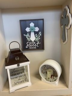 Decorative shelf with framed floral art, a small lantern, and a white round ornament on a cream background
