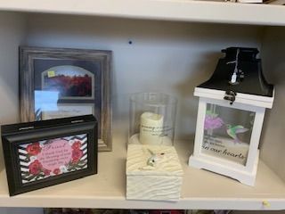 Shelf of framed decor, candles, folded towels, and a white wooden box with flowers and black ribbon