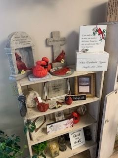 Small white shelf shrine with crosses, candles, flowers, framed note cards, and red decorative items