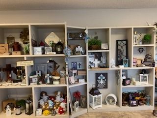 White wall shelves filled with assorted mini decor, framed art, plants, and jars in a cozy display room