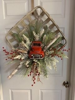 Christmas wreath with red toy truck, white frosted greenery, and berry accents on a white door