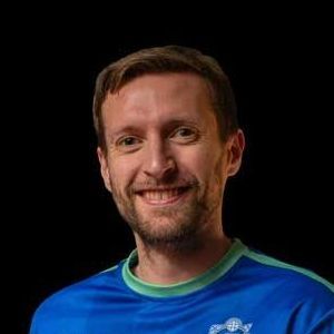 A man with a beard is wearing a blue shirt and smiling.
