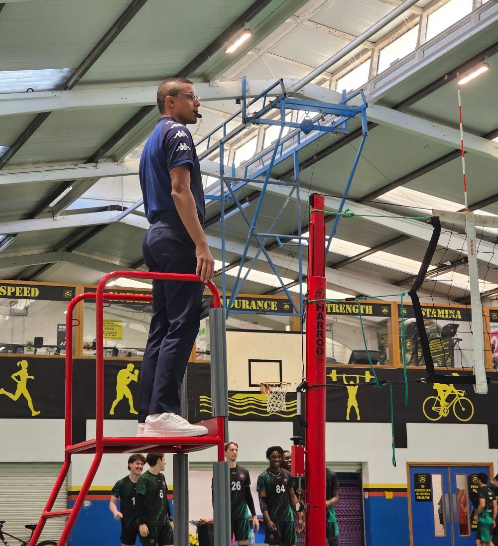 A man is standing on a basketball hoop in a gym.