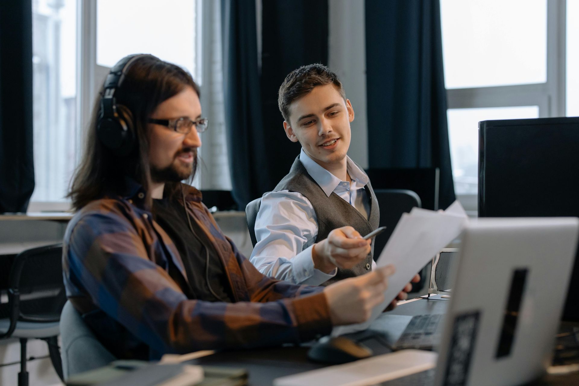 Two men are sitting at a help desk looking at a piece of paper.