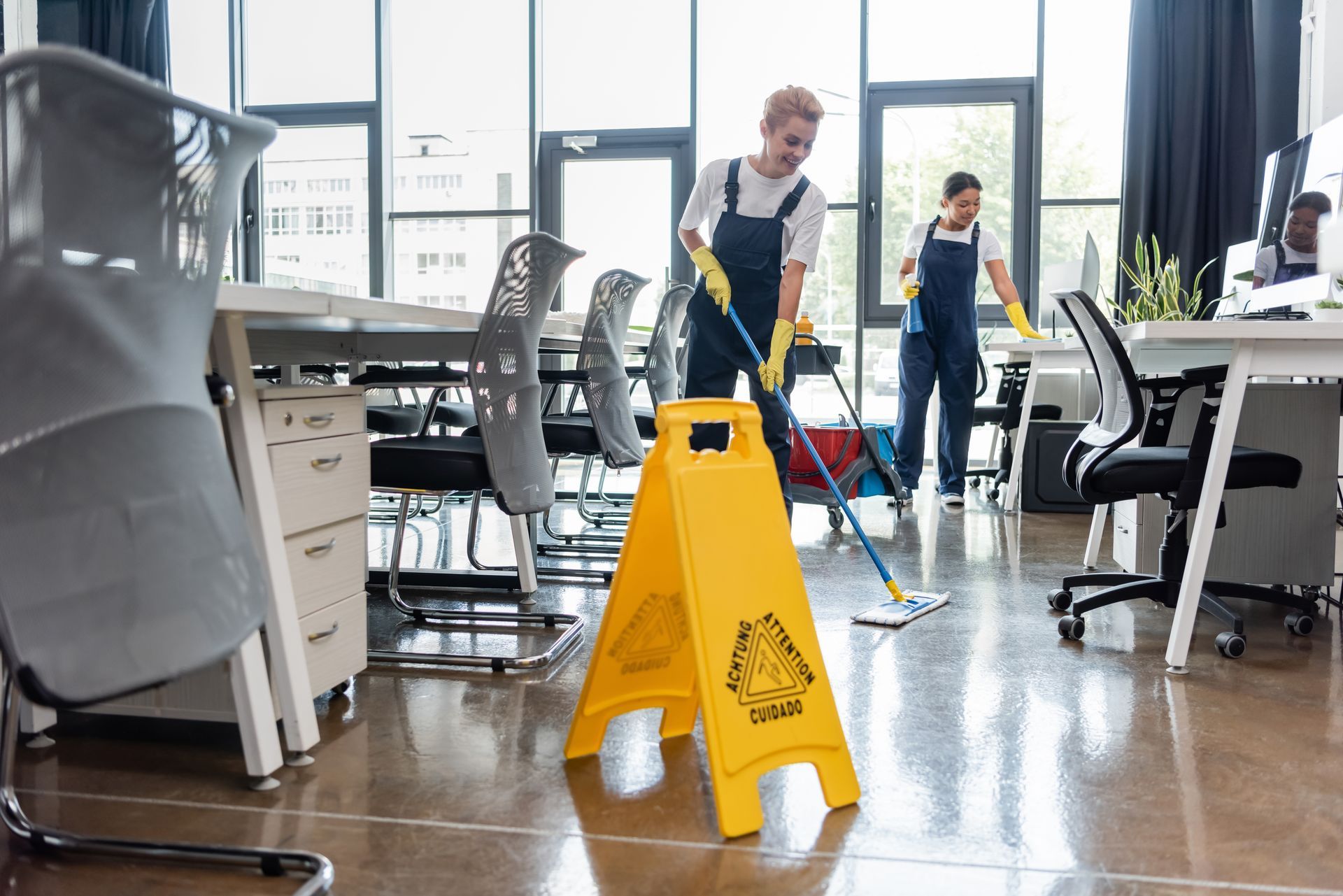 Two cleaners mopping an office floor, yellow caution sign in foreground.