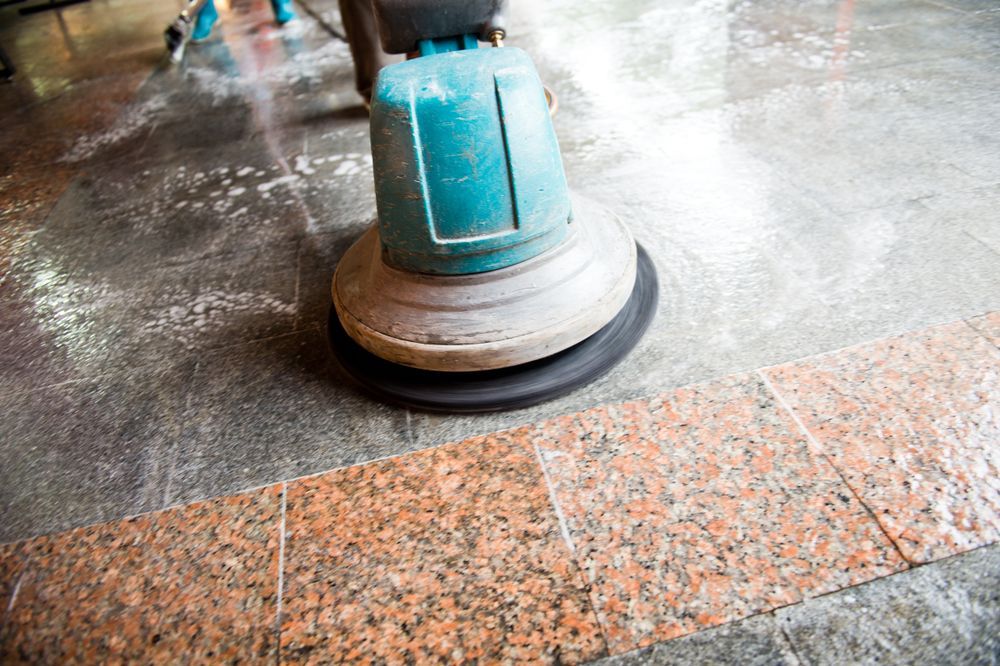Floor cleaning machine scrubbing a mottled floor with a red-brown border.