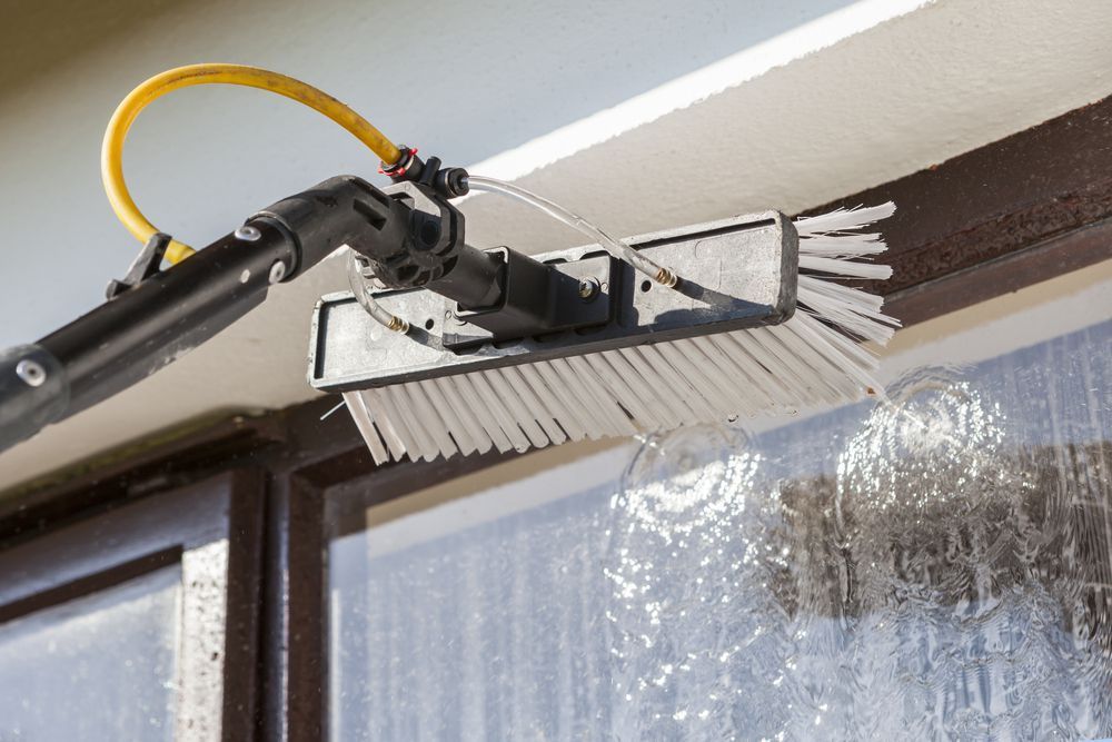 Window being cleaned with a water-fed pole system. Water sprays from brush across the window.